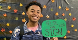 Kendall Johnson holding a sign that says "Rise and Sign"